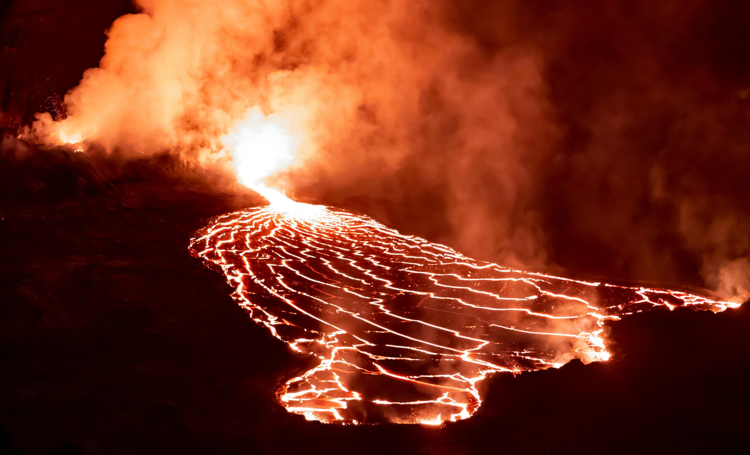 Dramatic view of a volcanic eruption at night with molten lava flowing and thick smoke rising.